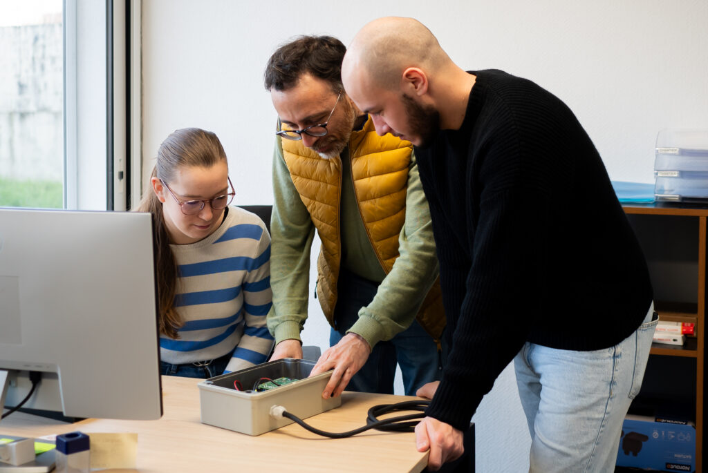 Équipe technique échangeant autour d'un coffret électrique au bureau d'études